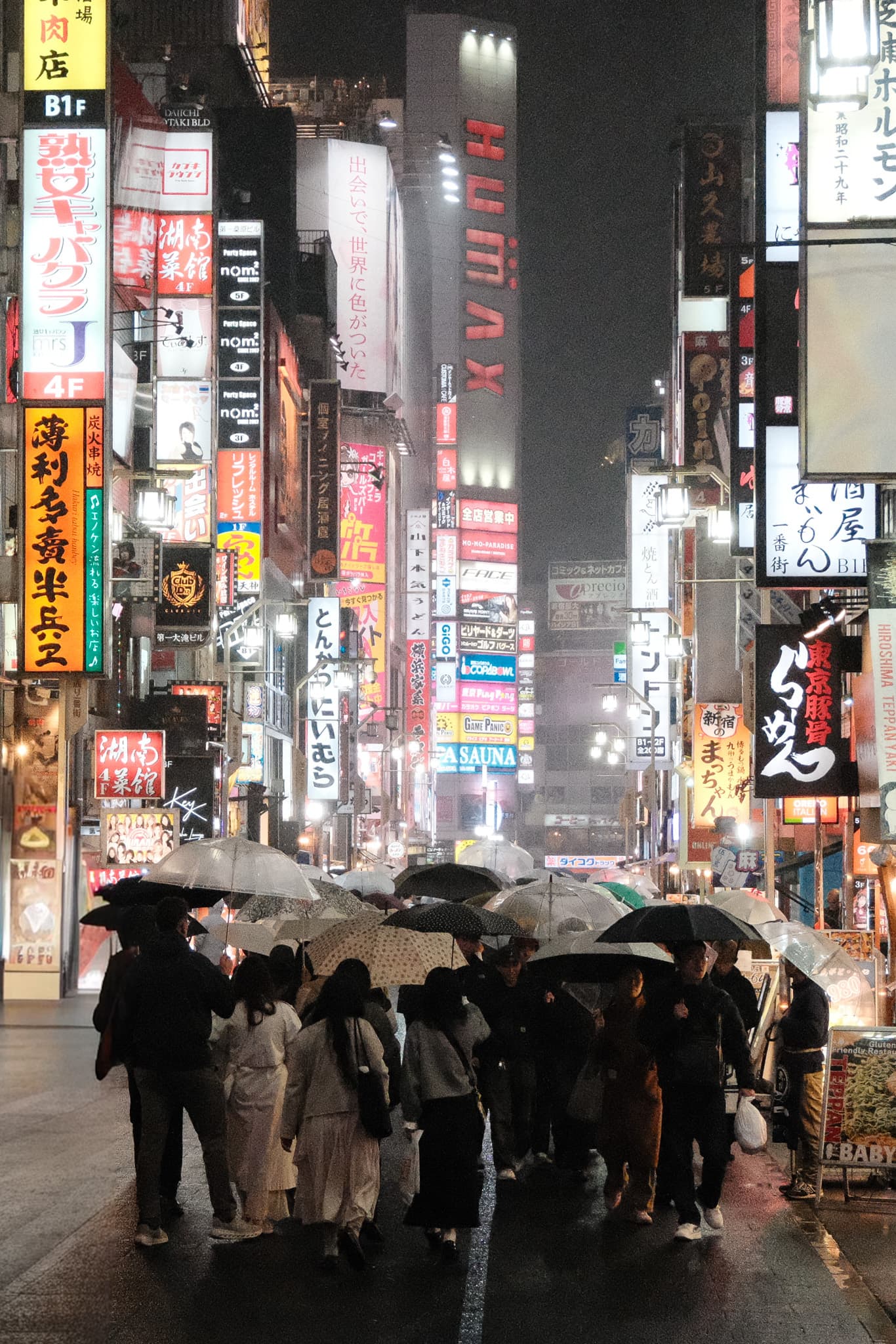 Umbrellas and pedestrians beneath illuminated city signs at night