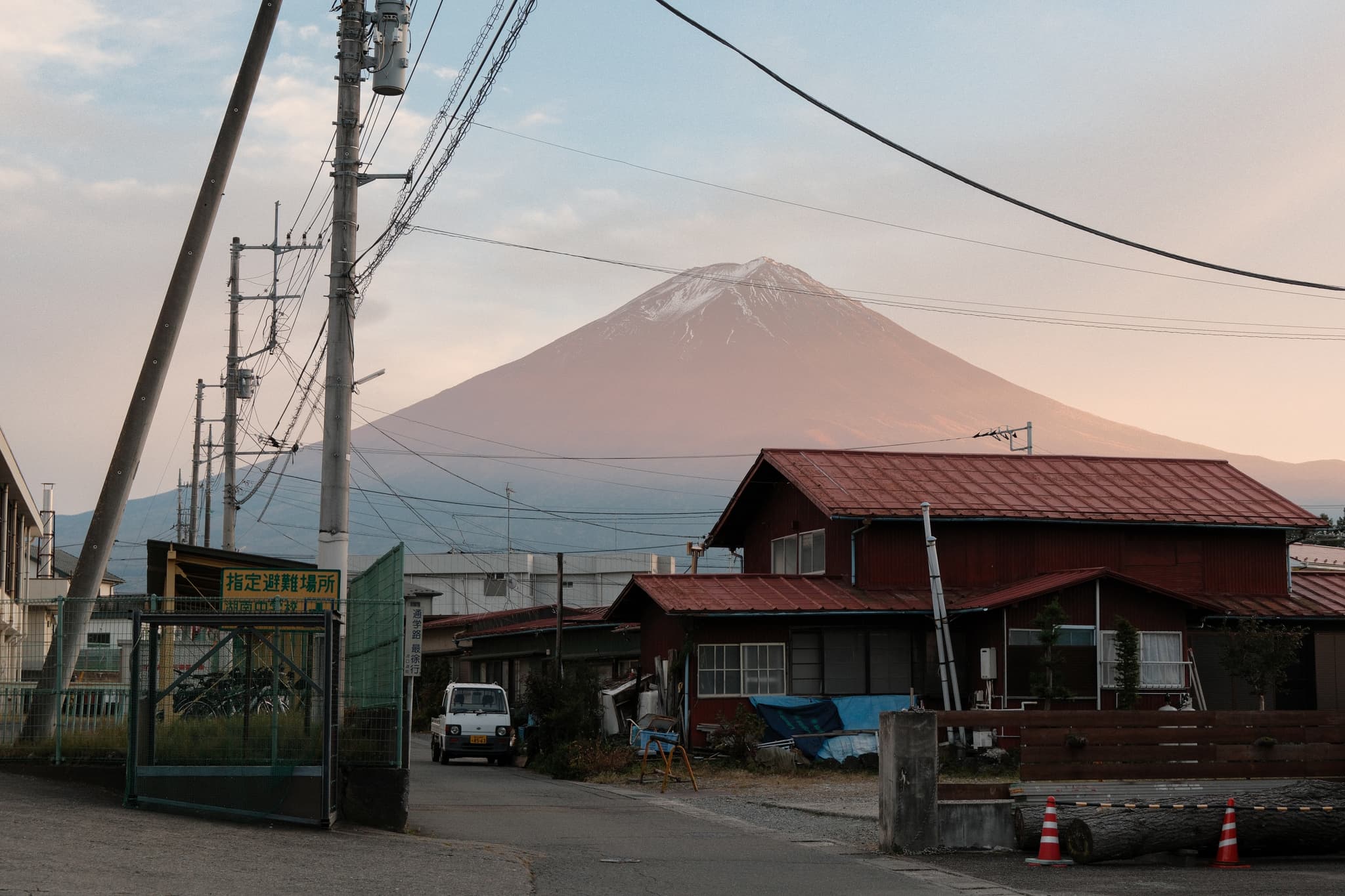 Mount Fuji above rooftops and power lines in soft evening light