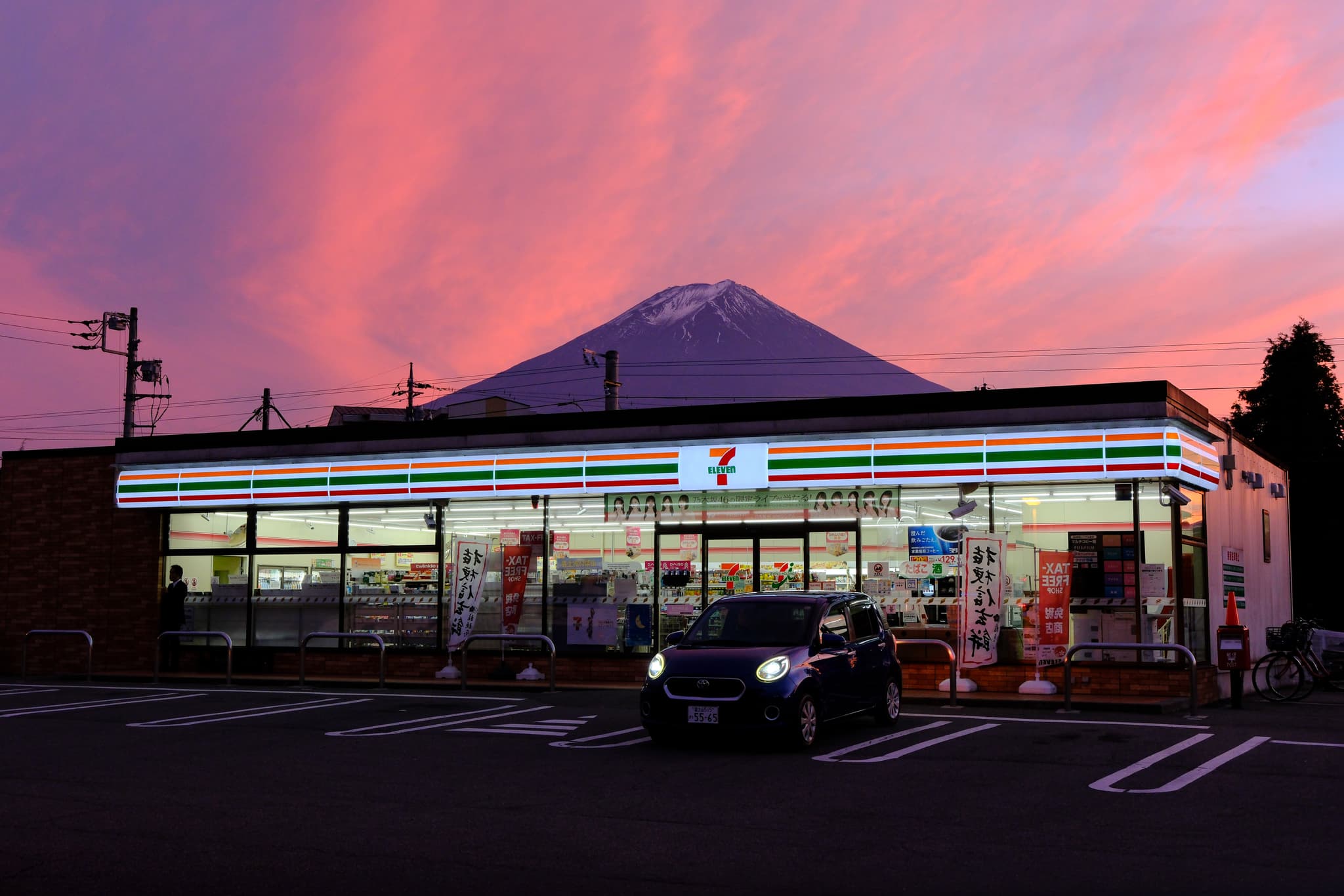 Mount Fuji beneath a pink evening sky behind a brightly lit convenience store