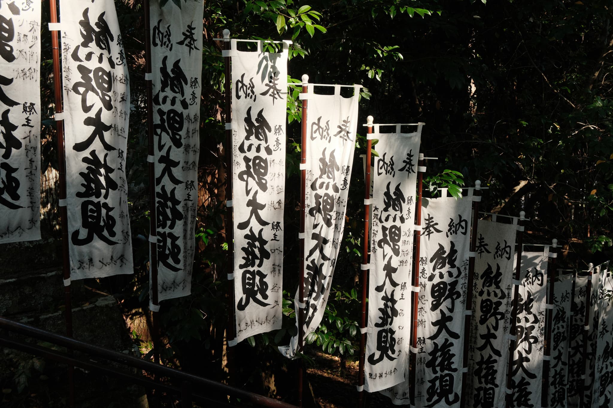 White banners with Japanese writing beside a wooded path