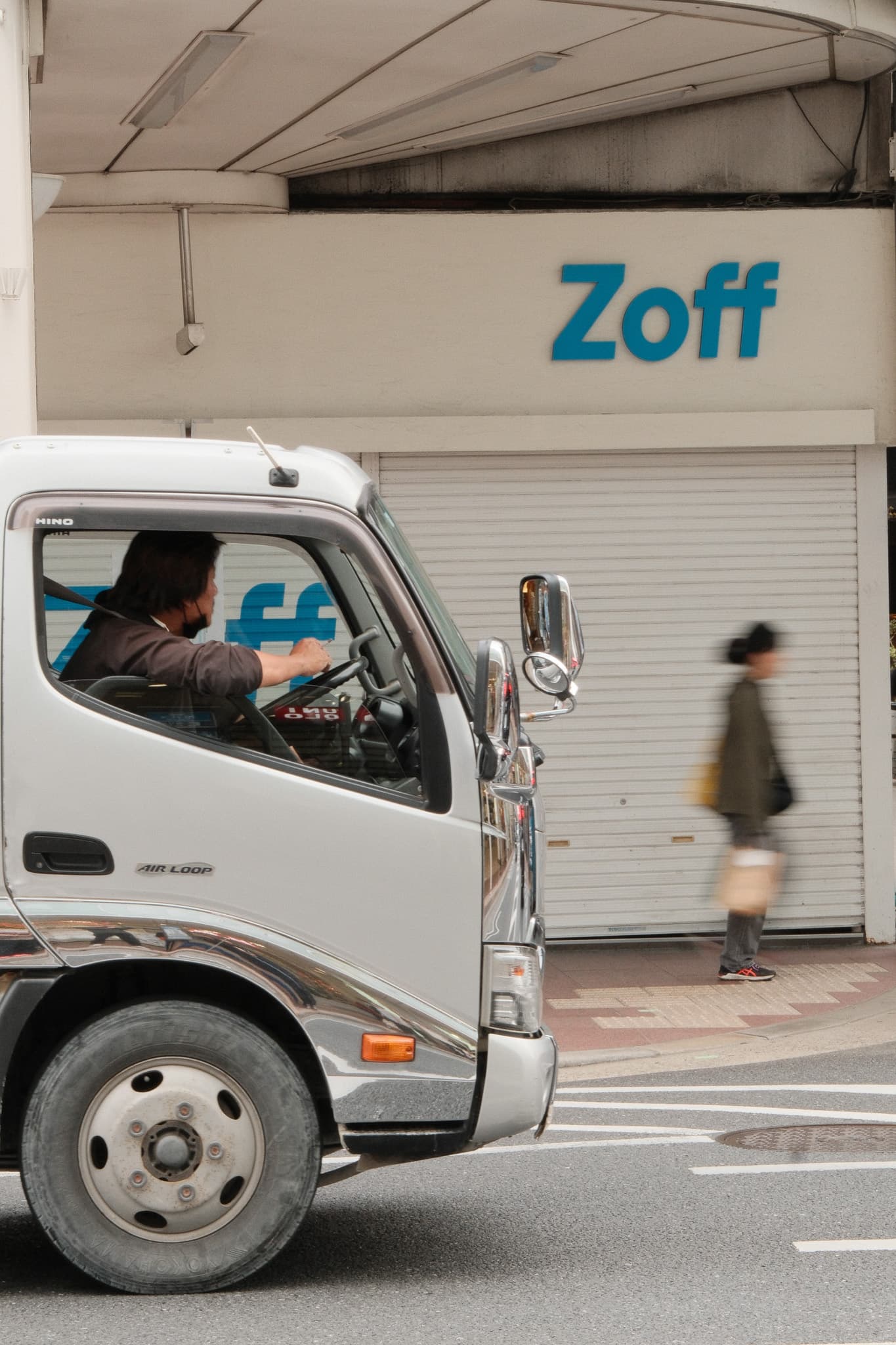 A pedestrian passing a small truck outside a storefront